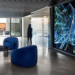 A person walking in a room with blue chairs and a large glass wall.